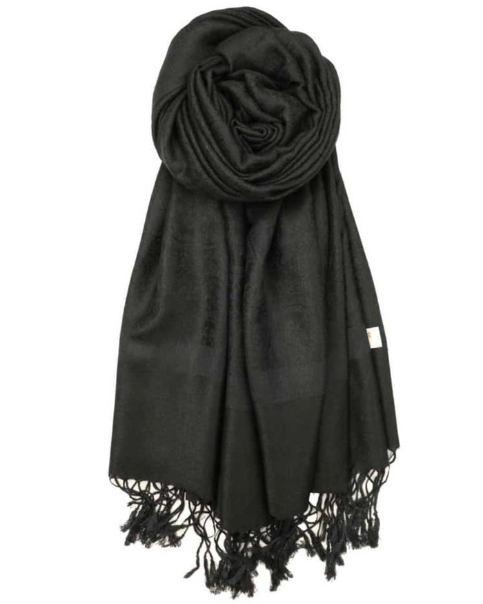 A black pashmina with paisley pattern and fringes spread out on a plain surface.