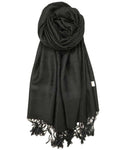 A black pashmina with paisley pattern and fringes spread out on a plain surface.