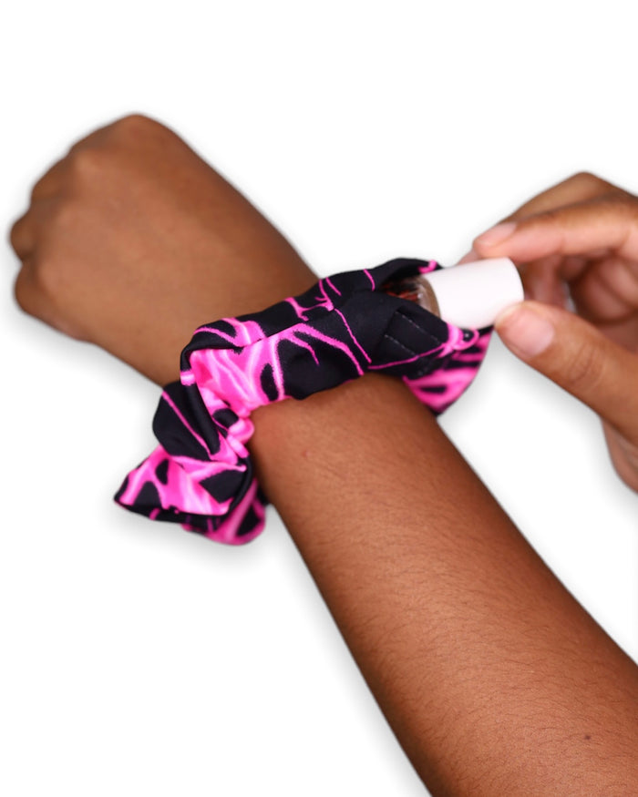 Pink Surge Stashie scrunchie hair tie with hidden velcro pocket opened on wrist with pink lighting bolts with a black background four way stretch polyester fabric.