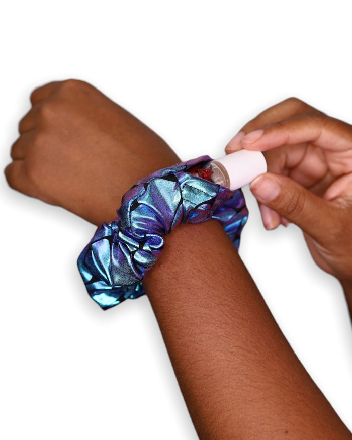 A close-up of the Poseidon Stashie being worn on the wrist, showing its iridescent blue and purple fabric with a hidden Velcro® pocket storing a lip balm.  One Stop Rave.